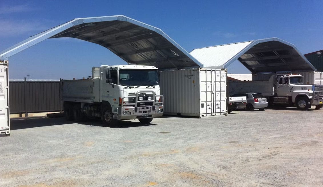 Open truck bays formed by white containers with metal gable roofs for vehicle shelter