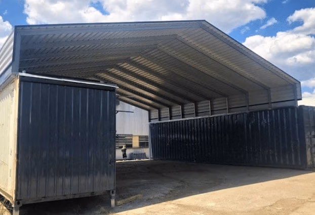 Large steel roof shelter structure built between two dark shipping containers